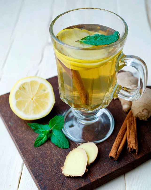 Sugar-free Ginger Cinnamon Tea - a clear glass mug filled with warm amber tea, garnished with a fresh lemon slice and a sprig of mint, sitting on a table ready to enjoy