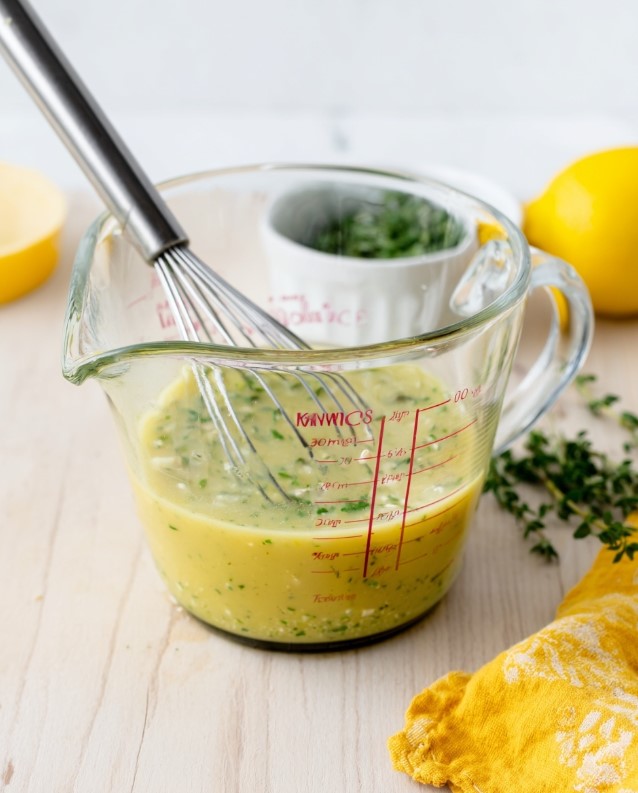 The dressing being whisked in a measuring cup to achieve a consistent texture before pouring.