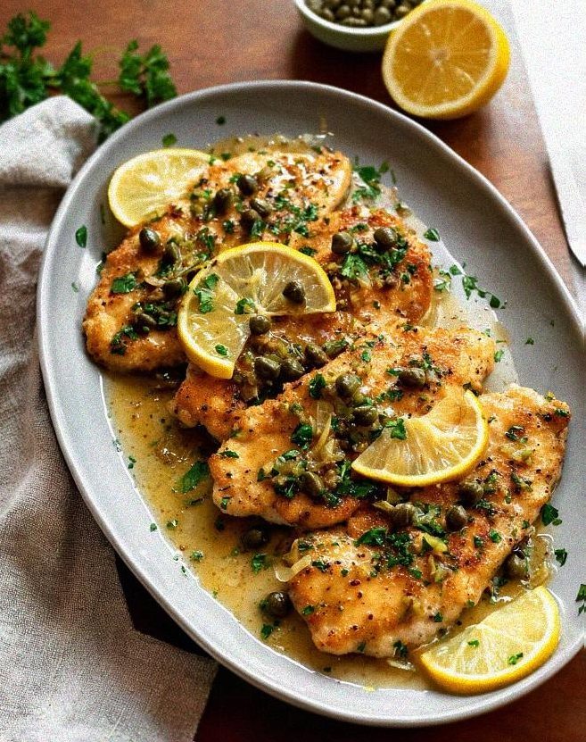 Browned chicken piccata in a ceramic baking dish covered with a glossy lemon caper sauce and fresh parsley