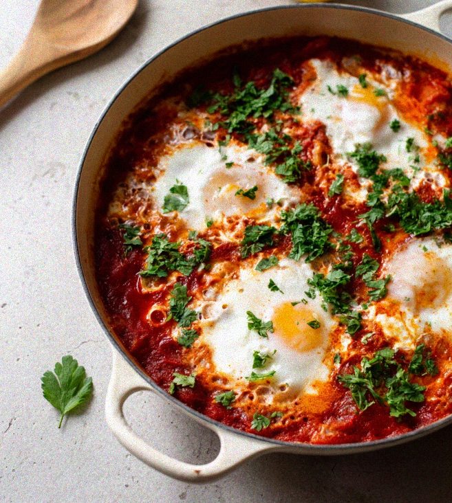 Smoked paprika shakshuka in an enamel skillet with softly poached eggs and fresh herbs